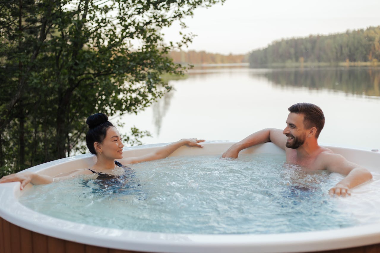 couple-looking-at-each-other-while-relaxing-in-a-jacuzzi-8844607 Couple enjoying a relaxing moment in an outdoor jacuzzi by a scenic lake at sunset.