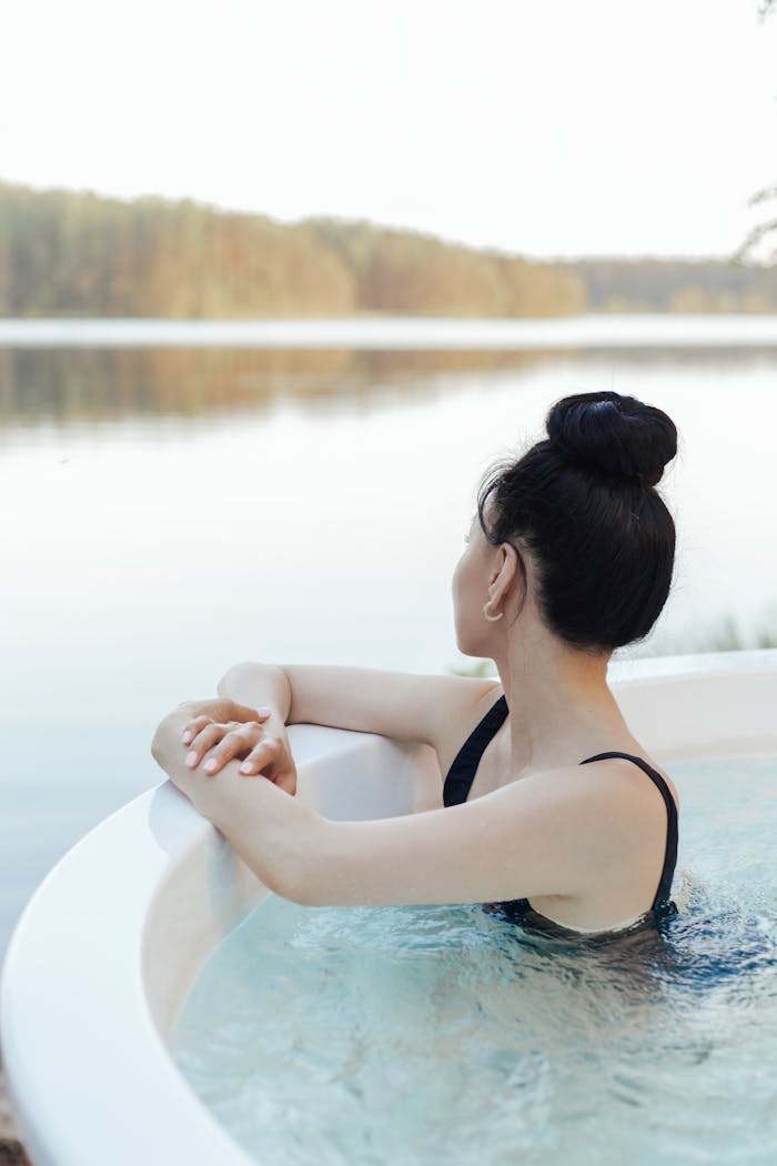 Woman relaxing in an outdoor jacuzzi overlooking a serene lake, embracing leisure and wellness.